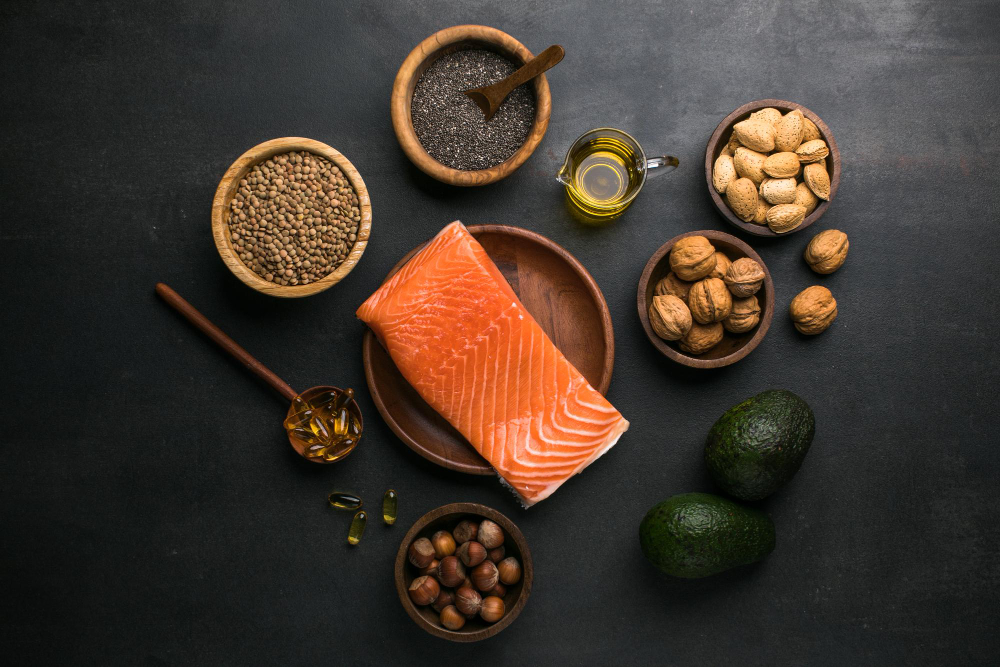 Kombinácia zdravých potravín odporúčaných pri andropauze: filet z lososa, avokádo, vlašské orechy, mandle, semienka a olej na tmavom podklade.