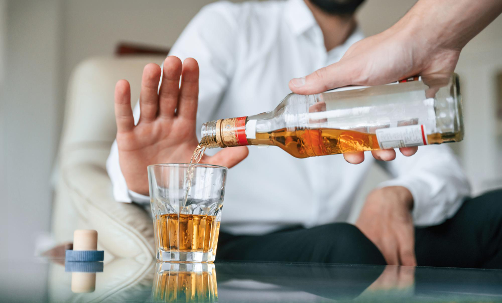 Muž odmieta pohár alkoholu, ktorý mu druhá osoba nalieva z fľaše