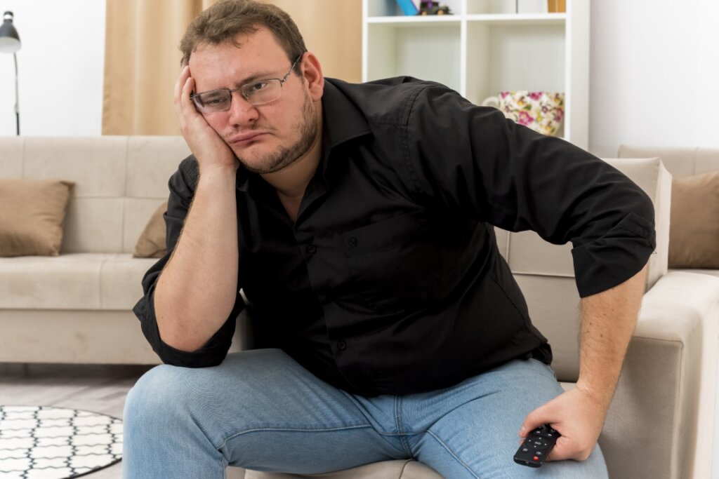 Obézny muž v čiernej košeli so smutnou tvárou sediaci na podlahe