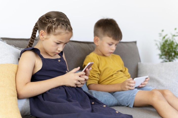 Deti sedia na pohovke a pozeraju do telefonov