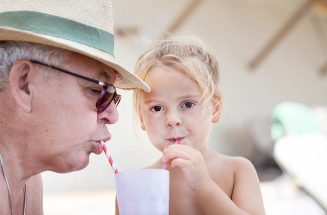 Little cute girl and grandfather drink cocktail through straw from one glass during summer vacation